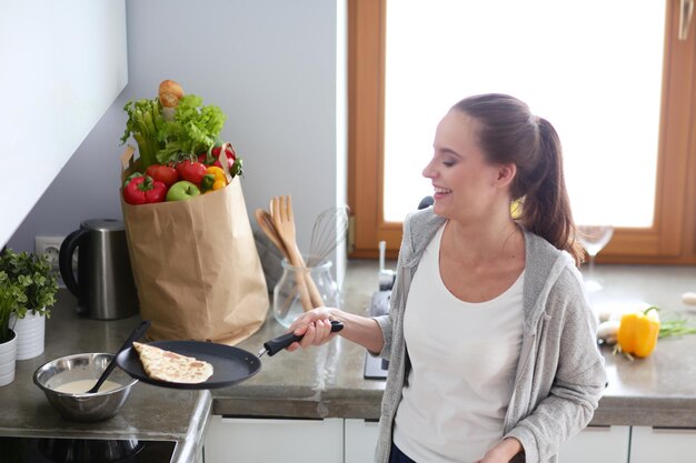 Young woman prepares pancakes in the kitchen while standing near the table Woman in the kitchen Cooking at kitchen