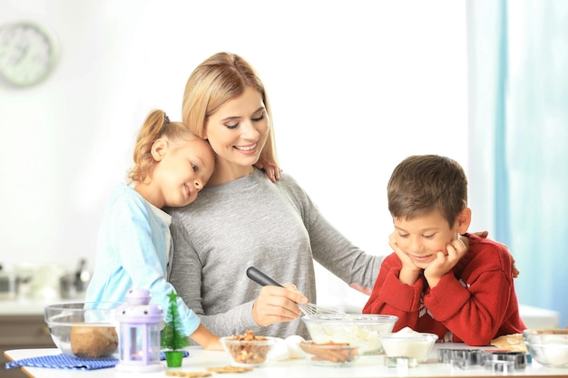 Young woman preparing Christmas cookies with little children in kitchen