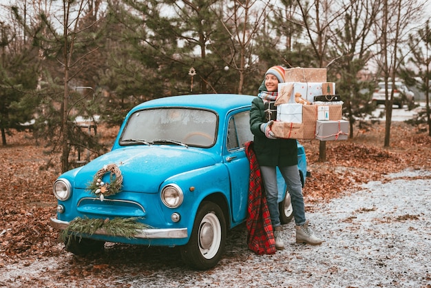 お祝いのクリスマスツリーbと青いレトロな車で飾られた休日のクリスマスプレゼントを準備する若い女性...