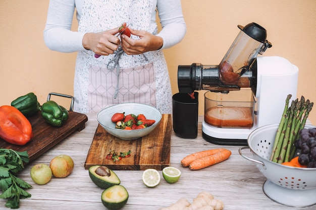 Giovane donna che prepara succo organico con la macchina dell'estrattore spremuto a freddo - ragazza che produce frullato con la verdura e la frutta