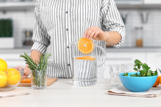 Young woman preparing tasty lemonade in kitchen