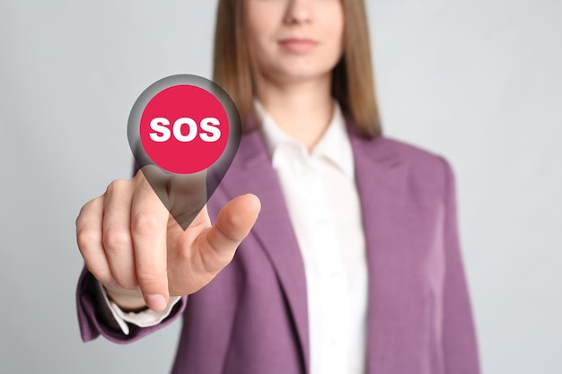 Young woman pressing virtual SOS button in case of danger on grey background closeup