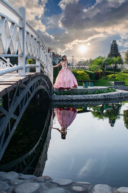 Young woman in a princess costume in the middle of a lake and a wooden bridge.