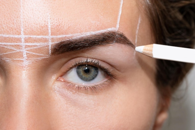 Young woman during professional eyebrow mapping procedure before permanent makeup