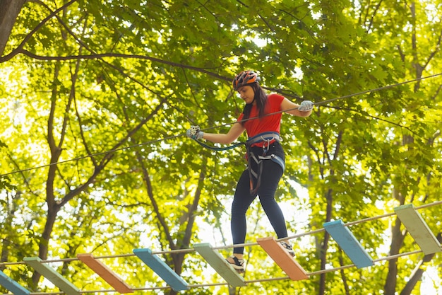 The young woman in protective gear steps on a suspension bridge The woman in protective gear is doing exercise in the rope park