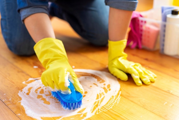 A young woman in protective gloves washes the floor with a brush and detergent