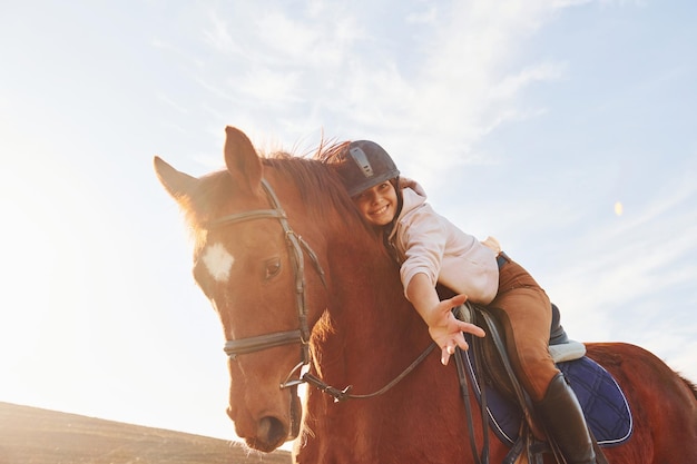 Photo young woman in protective hat with her horse in agriculture field at sunny daytime