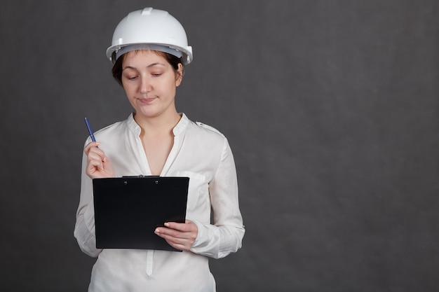 Young woman in a protective helmet with a tablet in her hands makes notes