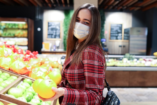 A young woman in a protective mask chooses fruit in the\
store