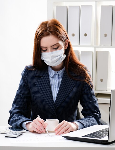 Young woman in a protective mask at the desk