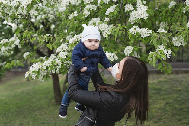 Young woman in a protective mask plays with her young son on the street. Covid-19