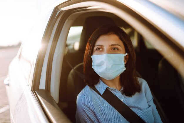 Young woman in a protective mask sitting in the car