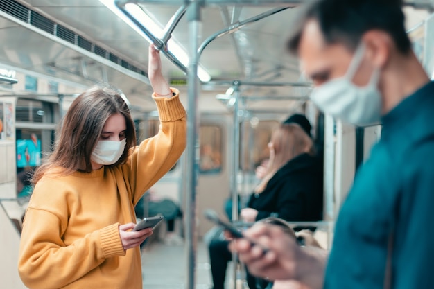 地下鉄の車に立っている保護マスクの若い女性。