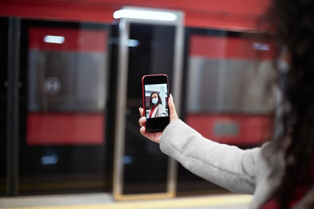 Giovane donna con una maschera protettiva che si fa un selfie mentre si trova in metropolitana