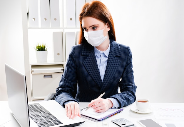 A young woman in a protective mask works on a computer.