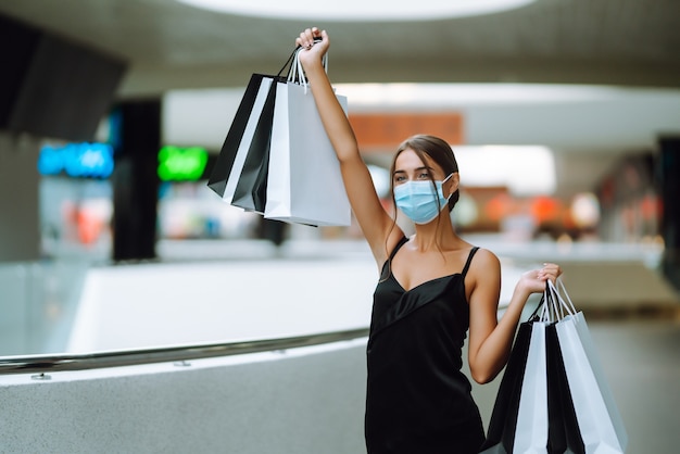 Young woman in protective sterile medical mask on her face with shopping bags in the mall.