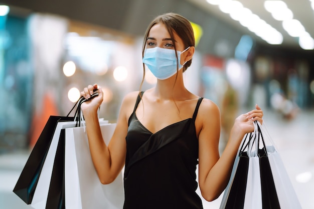 Young woman in protective sterile medical mask on her face with shopping bags in the mall.