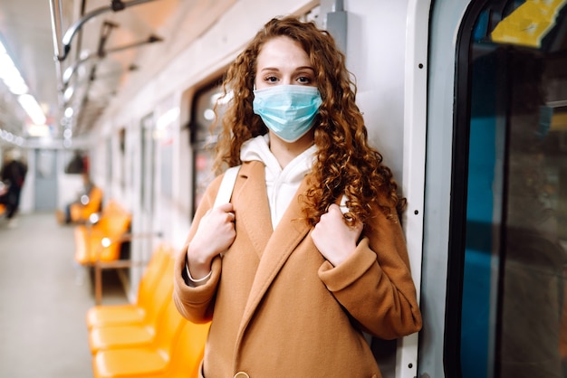 Giovane donna in mascherina medica sterile protettiva nel vagone della metropolitana