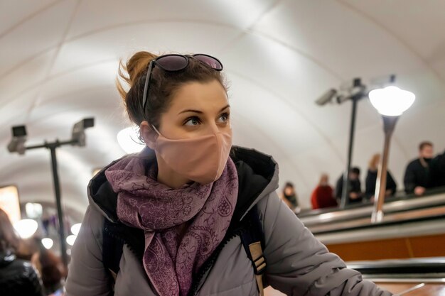 Young woman in protective sterile medical mask at subway escalator. Female wear face mask, protect from infection of virus, outbreak and epidemic in quarantine city