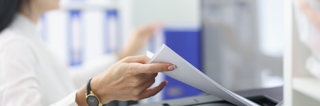 Young woman pulling paper out of printer closeup