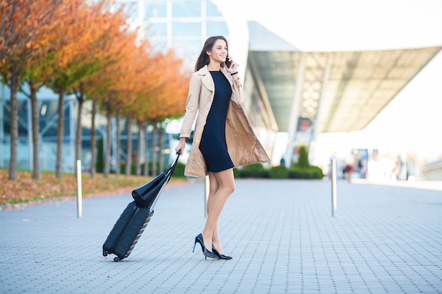 Young woman pulling suitcase near airport terminal.