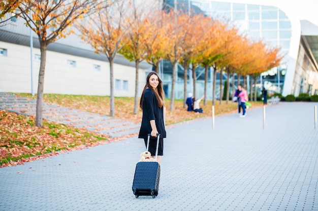Young woman pulling suitcase near airport terminal.