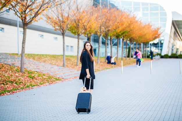 공항 터미널 근처 가방을 당기는 젊은 여자.