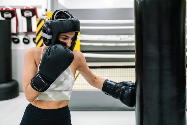 Young woman punching low a bag with boxing gloves in gym