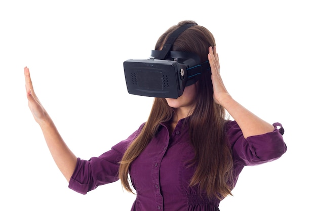 Young woman in purple blouse with long hair using VR glasses on white background in studio