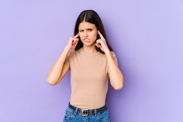 Young woman on purple covering ears with fingers, stressed and desperate by a loudly ambient.