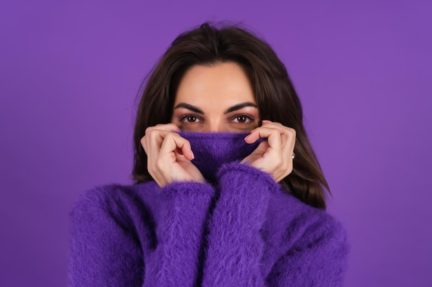 A young woman in a purple soft cozy sweater on the background is cute, in high spirits, looking at the camera with smiling eyes