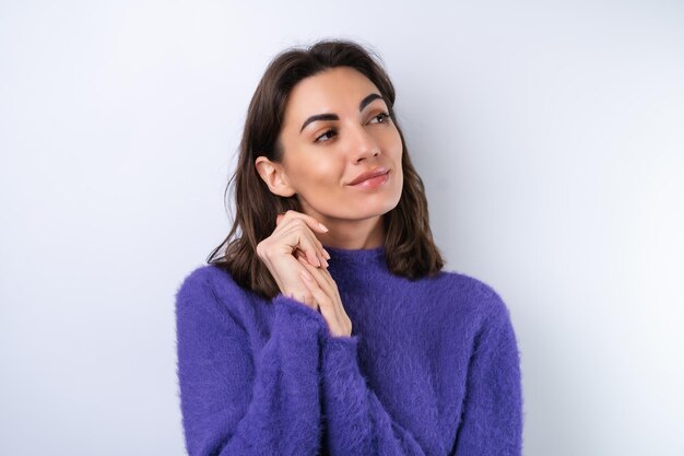 Young woman in a purple soft cozy sweater on the background thoughtful thinking  of ideas look aside