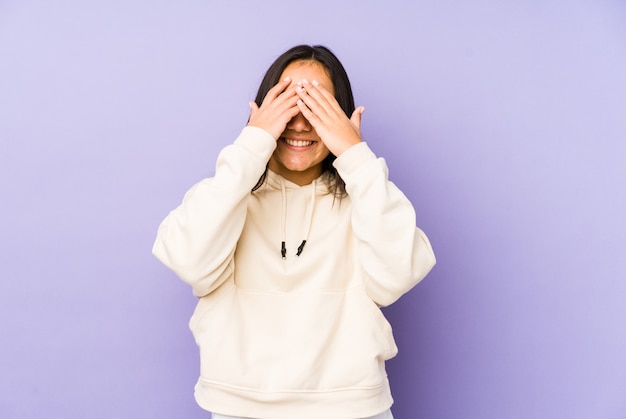 Photo young woman on a purple wall covers eyes with hands, smiles broadly waiting for a surprise.