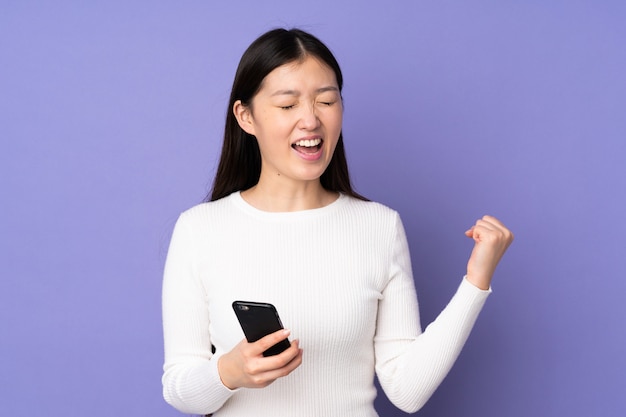 Young woman on purple with phone in victory position