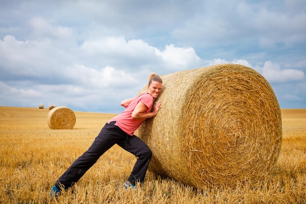 Young woman pushing in a field of straw bales