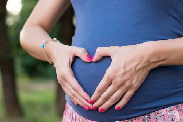 若い女性は、心臓の形を作る腹に彼女の手を置く