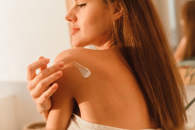 A young woman puts cream on her body in the bathroom Moisturizing the skin after a shower