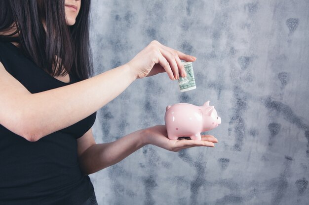 Young woman puts dollar in piggy bank