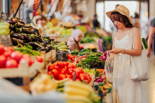 写真 若い女性は、食品市場で綿花の農産物の袋に果物や野菜を入れます。ショッピング用の再利用可能なエコバッグ。ゼロウェイストのコンセプト。