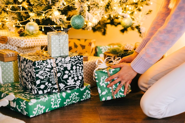 Photo young woman puts present under christmas tree while sitting on the floor at home.