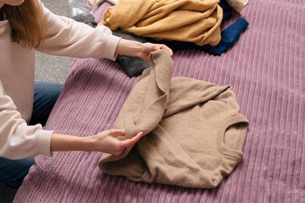 若い女性が暖かい冬のセーターを保管しています。ワードローブを一新し、古いものを新しいものに置き換えるというリサイクルと再利用のコンセプトです。