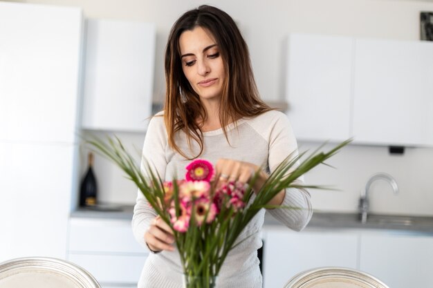 Молодая женщина кладет красочные цветы в вазу