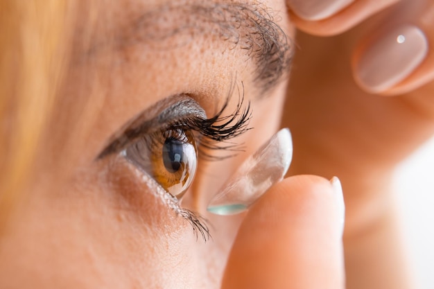 Young woman putting contact lens into her eye close up