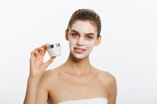 Young woman putting cream on her face isolated on white background