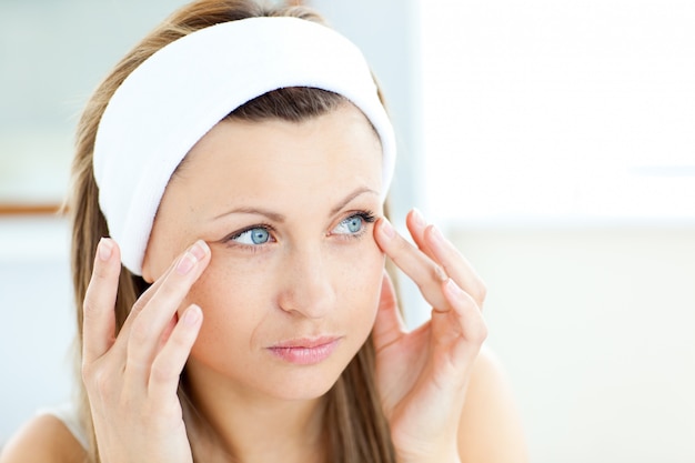 Young woman putting cream on her face wearing a headband in the bathroom