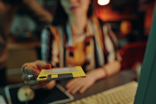 Young woman putting floppy disk in computer to read information while working at table