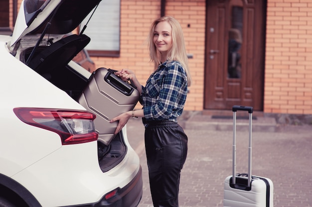 A young woman putting her luggage in the trunk of a car