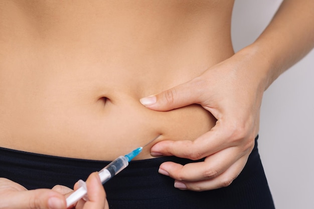 Young woman putting a hormonal injection in her stomach with the syringe The use of lipolytics