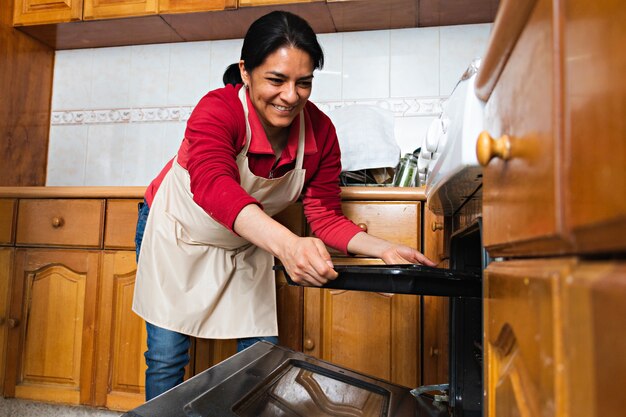 A young woman putting in the oven a metal tray with decorated\
raw dough, in a kitchen, she is wearing an apron