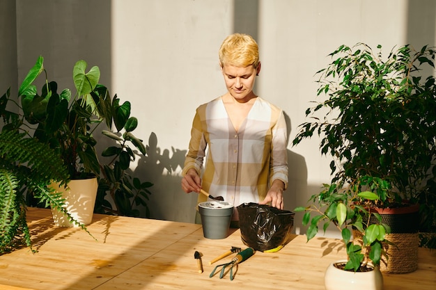 Фото Молодая женщина кладет почву в горшок, собираясь посеять растение в горшке
